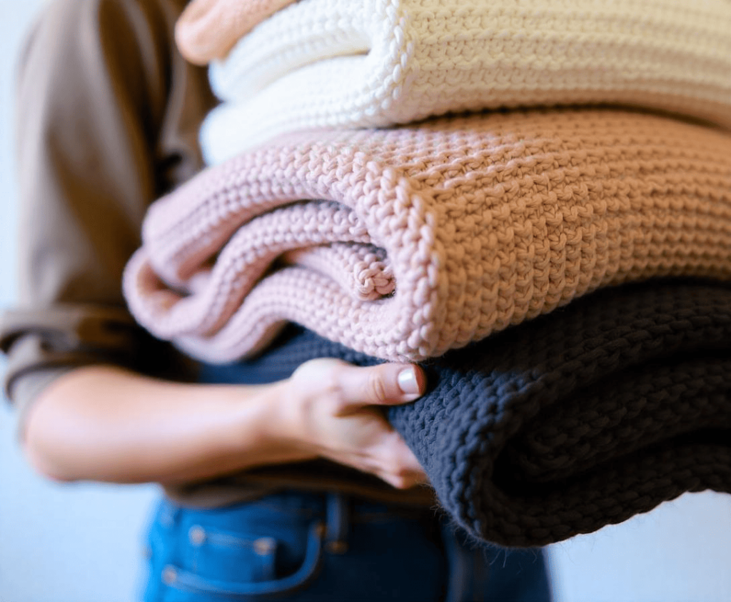 a-woman-holding-a-stack-of-folded-knitted-sweaters